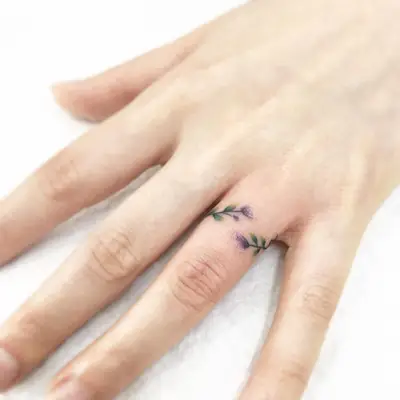 Person with dainty watercolor flower ring finger tattoo