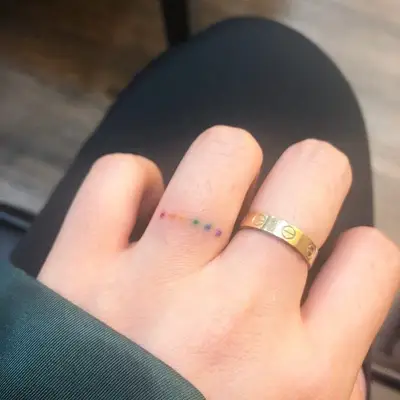 Person with a rainbow dotted ring finger tattoo