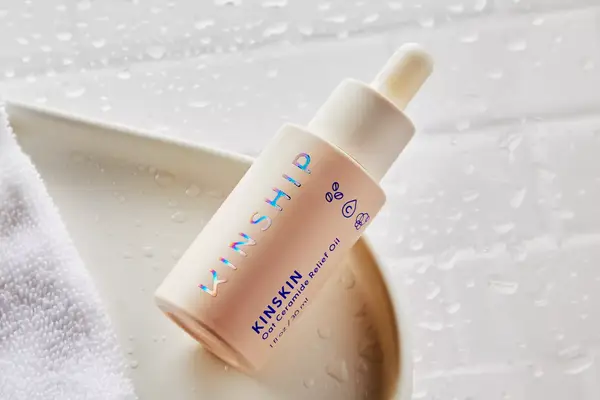 Kinship Kinskin Ceramide Barrier Repair Oil displayed on white tray with nearby towel