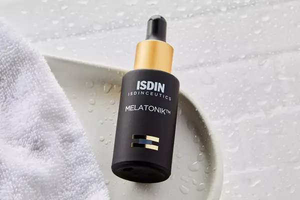 Isdin Isdinceutics Melatonik Overnight Recovery Serum displayed on wet tile with nearby white cloth