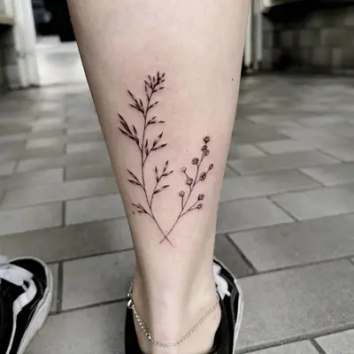 Lower calf tattoo of branches with negative space leaves and blooms