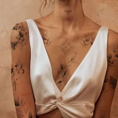 zoomed in image of model with fine line tattoos on chest, neck, and collarbone - thin line work, dainty flowers and shapes