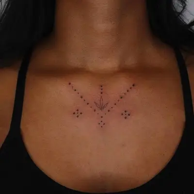 zoomed-in image of model with black ink dot work tattoo in center of collarbone with small dots and leaf shape