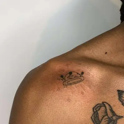 zoomed-in image of model with stick and poke style tattoo with a UFO and three aliens