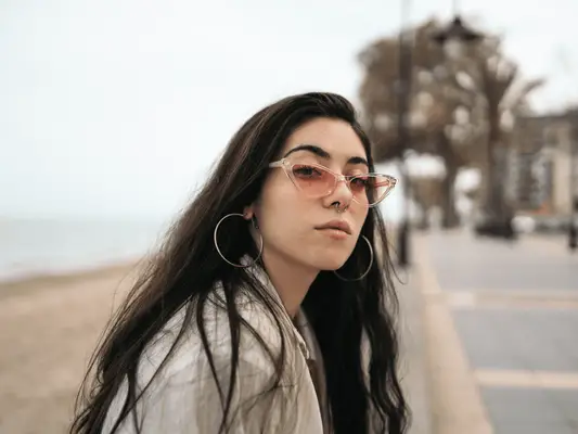 A woman with a septum piercing and sunglasses sitting outside