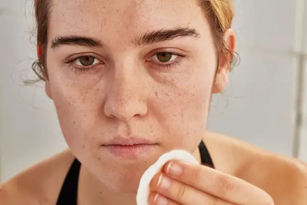 Person applying micellar water to their chin with a cotton round