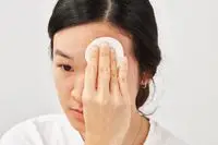 Person applying micellar water to their face with a cotton round