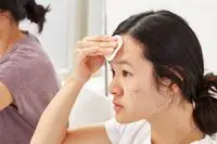 Person removing eye makeup from their eyes with a micellar water soaked cotton round