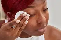 Person removing eye makeup with a cotton round