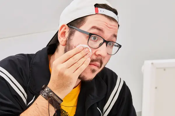 Person wiping cheek with a cotton round of micellar water