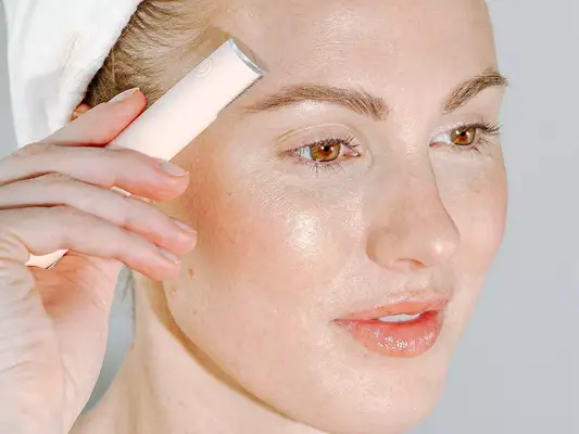 woman dermaplaning face against gray background