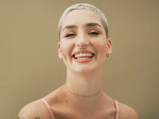 Close up of a woman with a blonde buzz cut and lip and nose piercings.