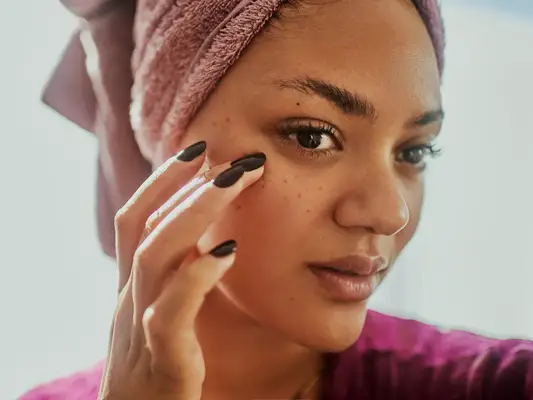 A woman with her hair wrapped in a towel as she touches her face