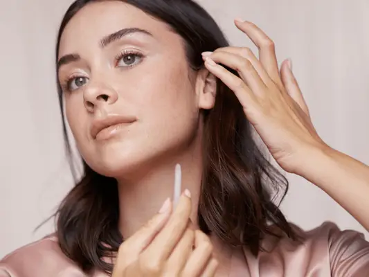 A woman holding a gua sha in her hand as she pulls her hair back revealing a sharp jawline