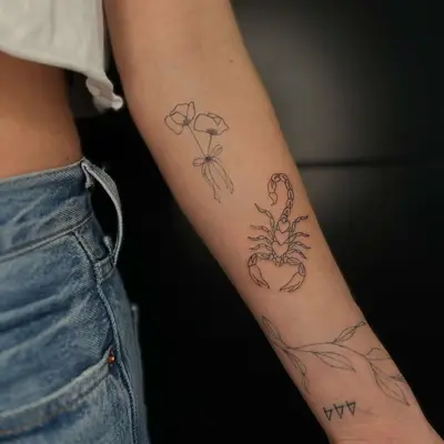 An arm with patchwork tattoos including flowers, a scorpion, leaves, and 444