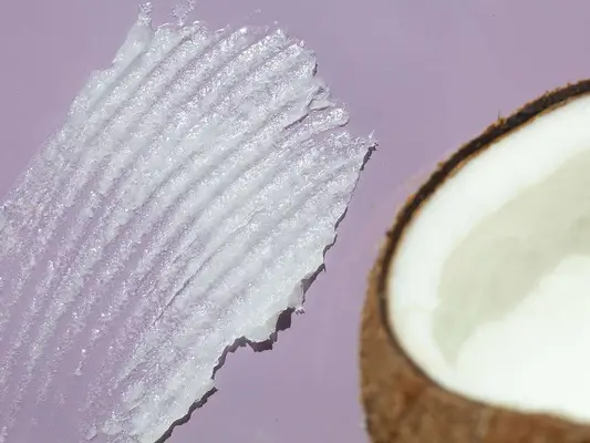 A swatch of coconut oil beside a coconut on a purple background