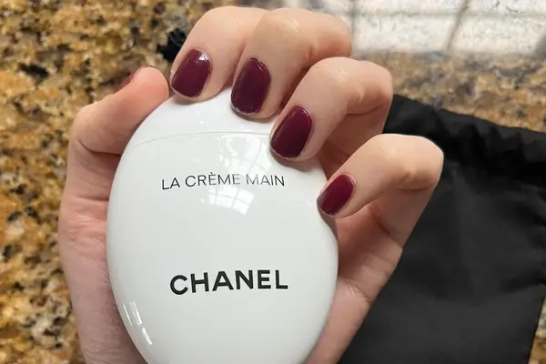 A hand with manicured nails holding the Chanel La Crème Main