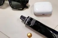 Close up the Grown Alchemist Hand Cream Vanilla Orange Peel on a case near sunglasses and AirPods Pros