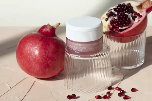 Pomegranates and pomegranate seeds flank a pink skincare product
