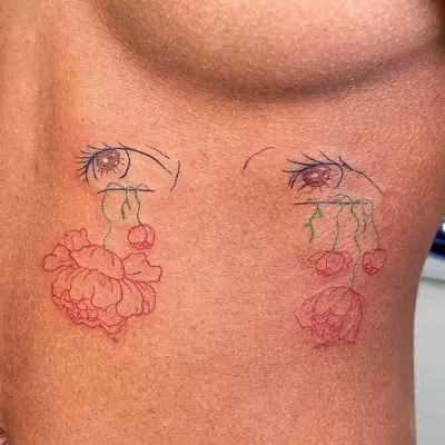 Close-up of colorful fine line tattoo with blue lashes, brown irises, and red and green flowers