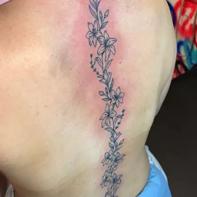 image of black ink fine line tattoo of flowers and vines going down spine