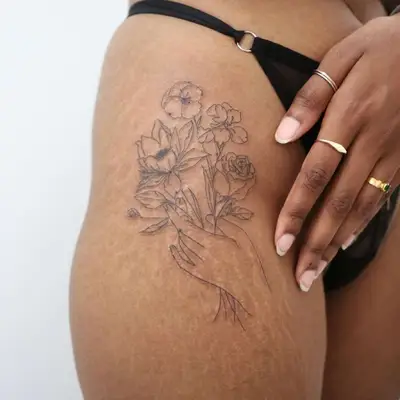 Close-up of fine line floral bouquet in hand tattoo on upper outer thigh