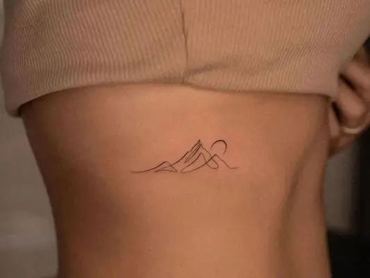 Close-up of fine line mountain and moon tattoo on ribs