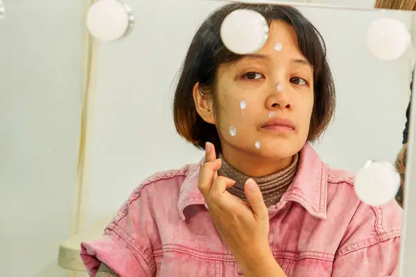 Face reflected in mirror as hand dots sunscreen onto it