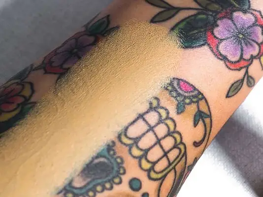 Close up of a tattooed forearm, a swatch of foundation down the center