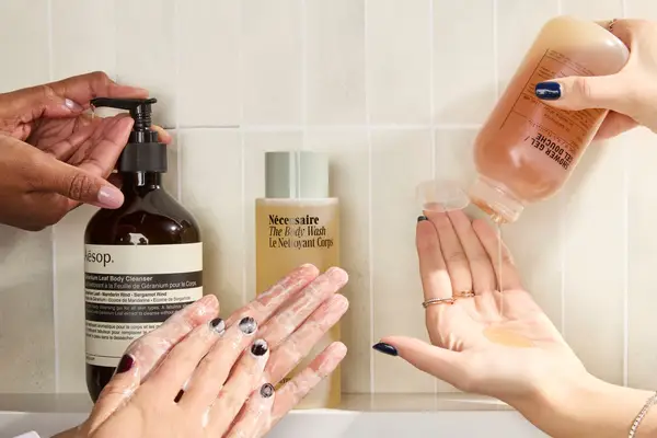 A collage of three sets of sudsy hands trying body washes from Aesop, Necessaire, and Le Labo