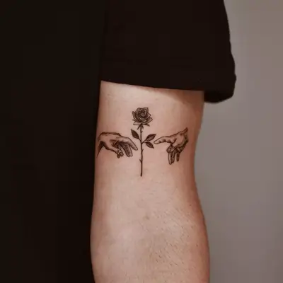 Close up of an arm tattoo that is two hands reaching in the middle towards a rose,