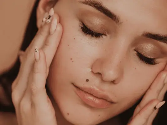 Close up of a model closing their eyes, showing clear skin with freckles. 