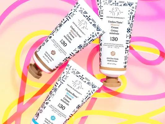 Drunk Elephant Umbra Mineral Cream sunscreens on a colorful background