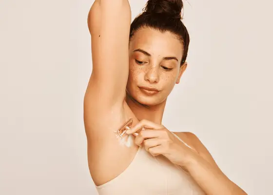 Woman lifting her arm while shaving her armpit 