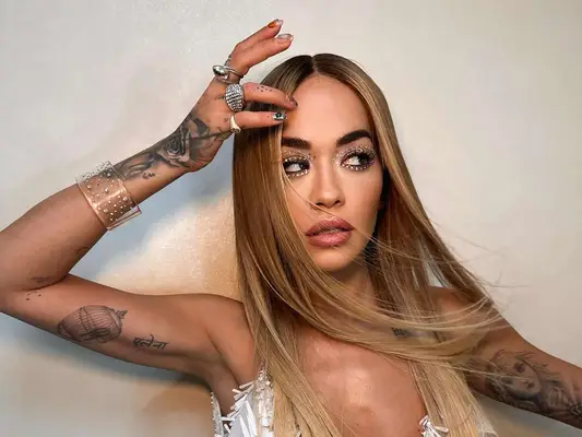 Singer Rita Ora, hand on her forehead, multiple tattoos visible