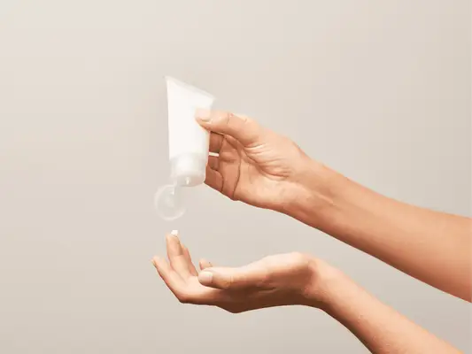 Two hands, one holding a white skincare tube and squeezing out product onto a finger on the other hand