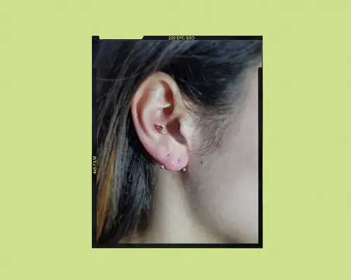 An ear with hair tucked behind it displays a transverse lobe piercing