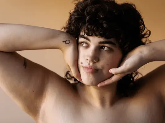 Close up of a brown curly-haired woman with two arm tattoos.