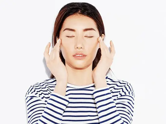 A woman in a striped shirt using her hands to give herself a facial massage