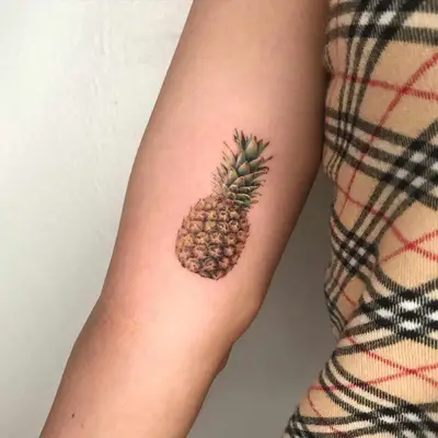 Close-up of arm with realistic pineapple tattoo near side elbow