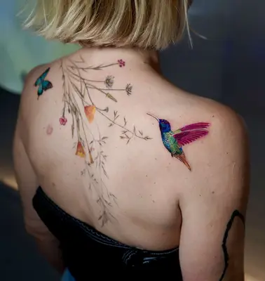 A colorful hummingbird back tattoo, which is next to a big flower tattoo