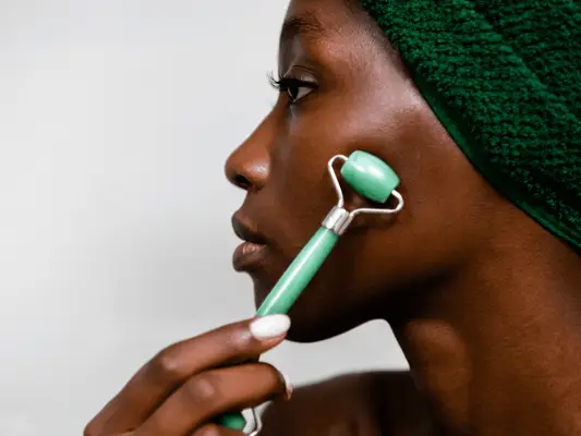 woman using a jade roller on cheek