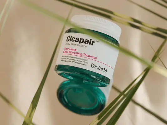 A jar of Dr. Jart Tiger Grass Color Correcting Treatment Cream surrounded by pieces of grass