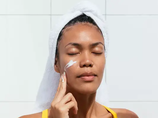 woman with hair in towel applying moisturizer to face