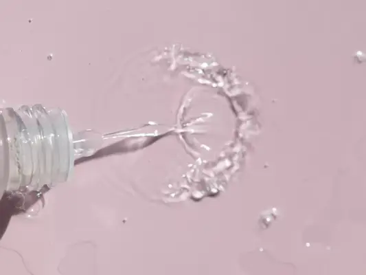 Close up of a bottle of liquid being squirted on a pink background