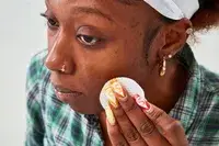 Person using a cotton round on their cheek