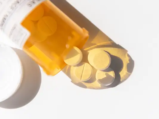 An orange pill bottle with white circular pills spilling out.
