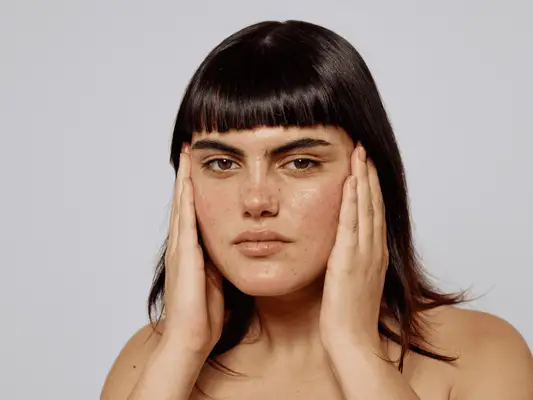 A woman with bangs touching her face with her hands