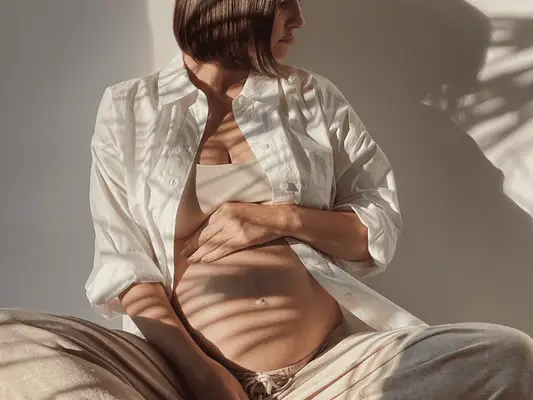 A pregnant woman sitting and holding her belly with her shadow projected on the wall