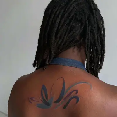 Back view of watercolor graphic shoulder tattoo on dark skin